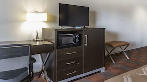Une pièce de taille modeste comprenant un bureau, une chaise, un meuble avec un four à micro-ondes et un téléviseur.