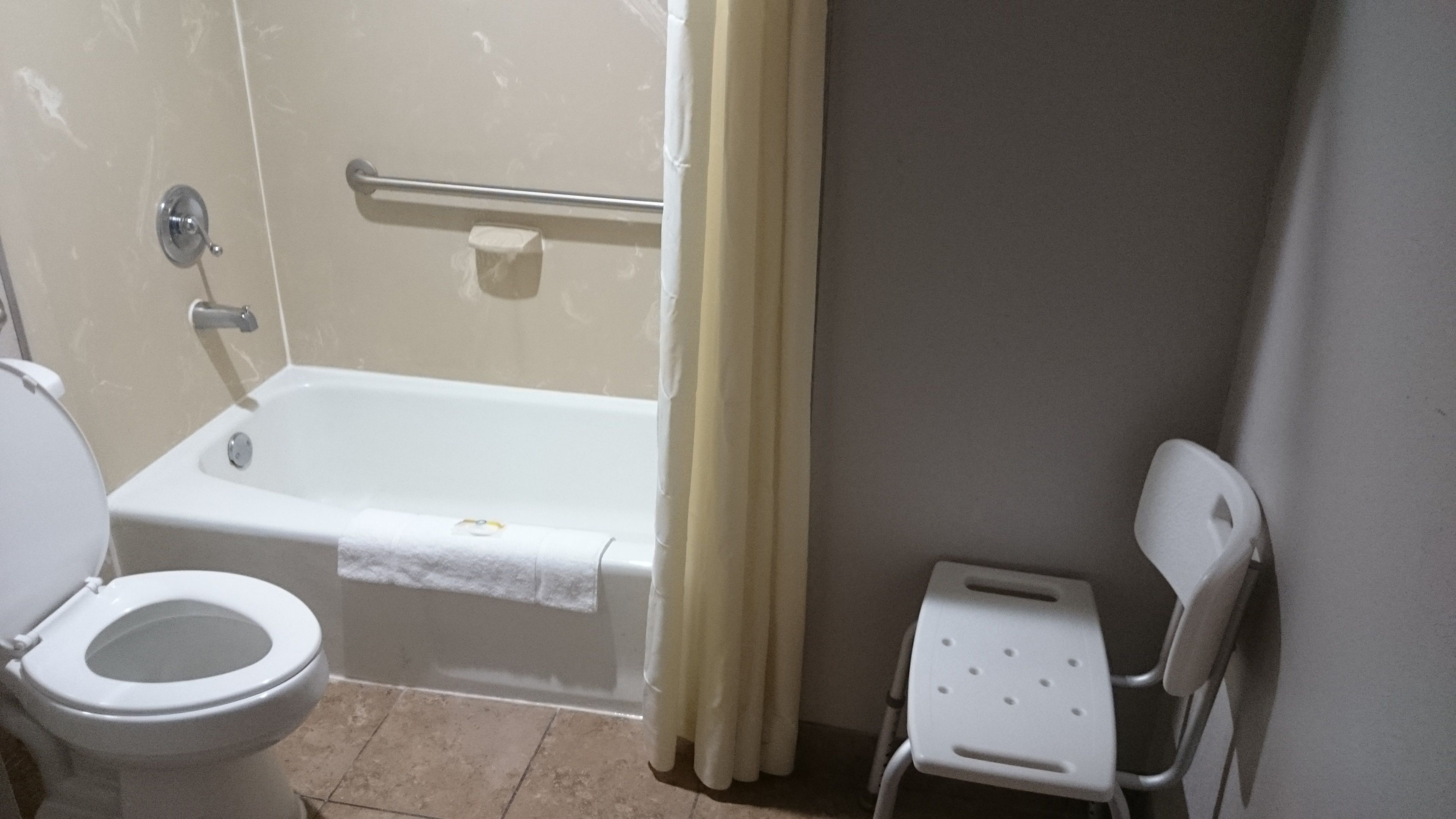 A bathroom with a bathtub, toilet, and a small white chair.