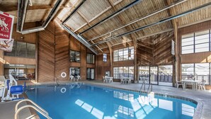 Une piscine intérieure aux murs et au plafond en bois, entourée de tables et de chaises.