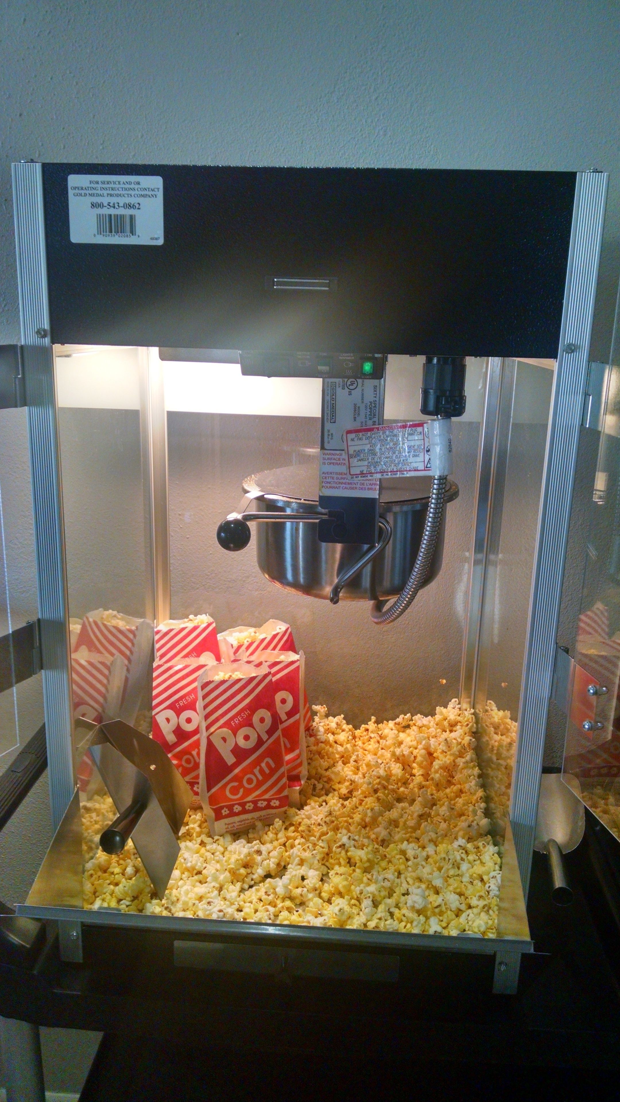 Una macchina per popcorn con un contenitore metallico pieno di popcorn, una scatola per popcorn e un mestolo di metallo.