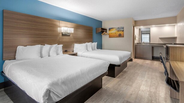 A hotel room with two beds, a kitchenette, and a painting on the wall.