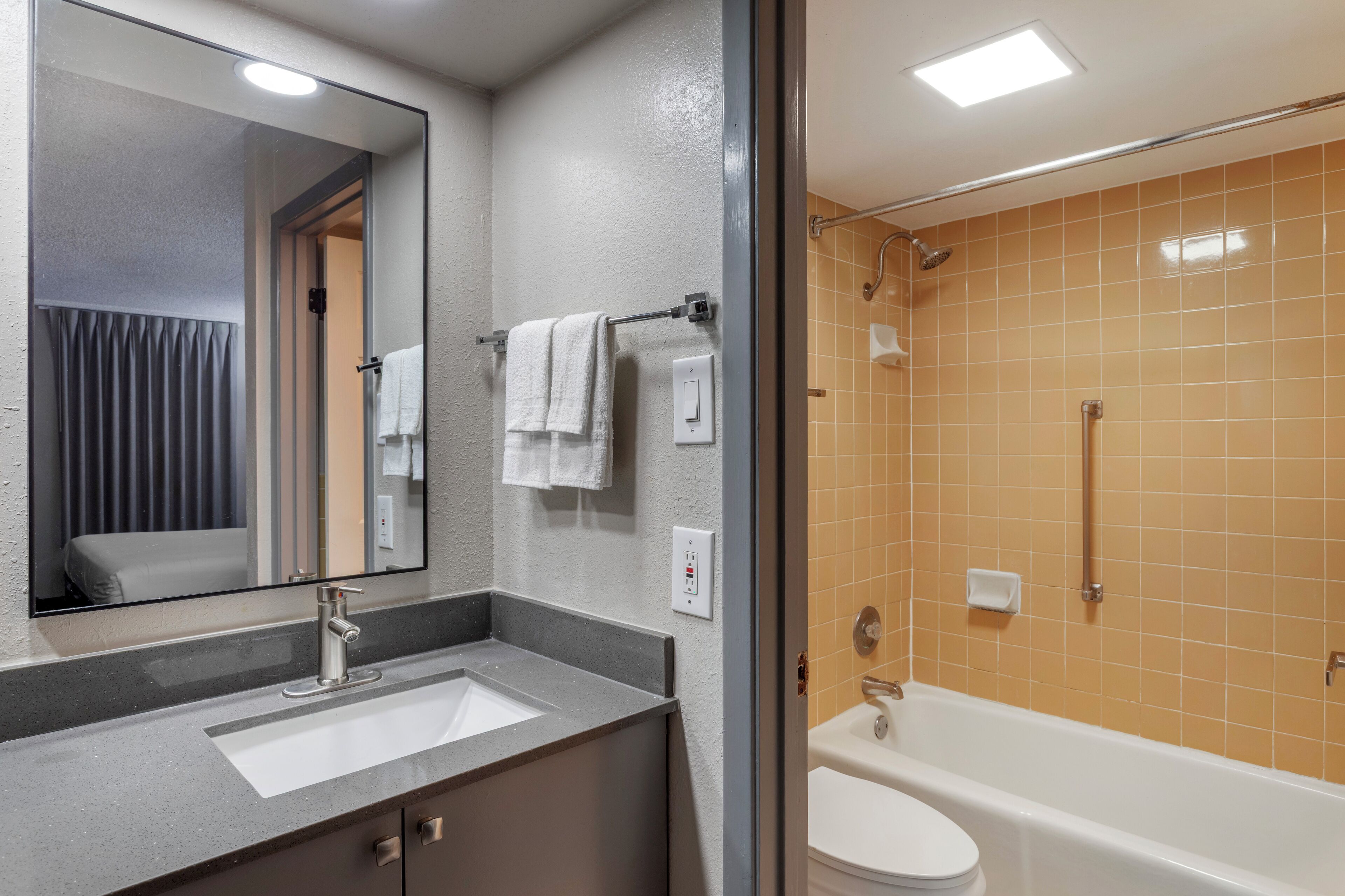 Un baño con lavamanos, espejo, toallero y bañera.