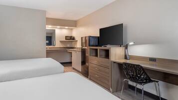 A compact hotel room with a kitchenette, a bed, a desk with a chair, and a TV.