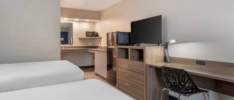Ein kompaktes Hotelzimmer mit Küchenzeile, einem Bett, einem Schreibtisch mit Stuhl und einem Fernseher.