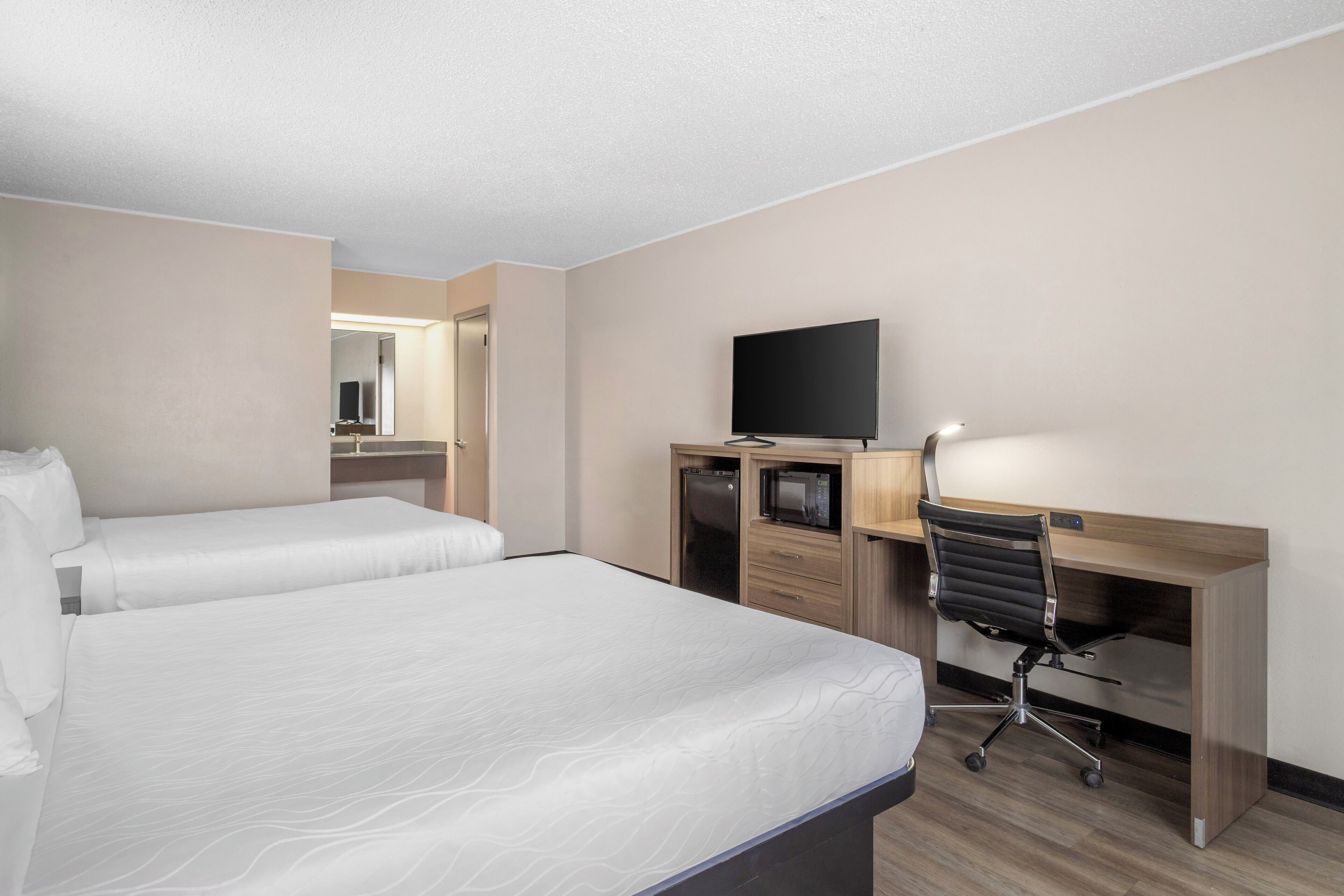 A hotel room with two beds, a desk with a chair, a television, and a microwave.