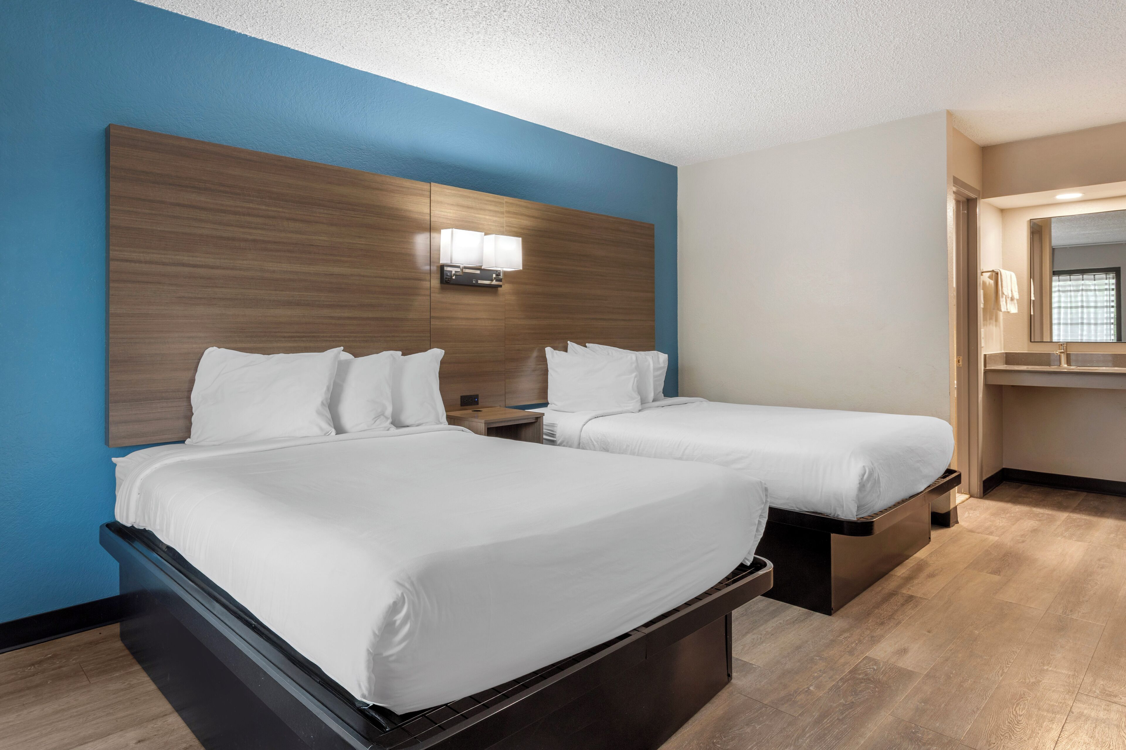A hotel room with two beds, a wooden headboard, a nightstand, a mirror, and a wooden floor.