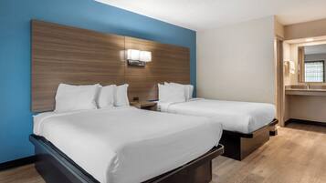 A hotel room with two beds, a wooden headboard, a nightstand, a mirror, and a wooden floor.