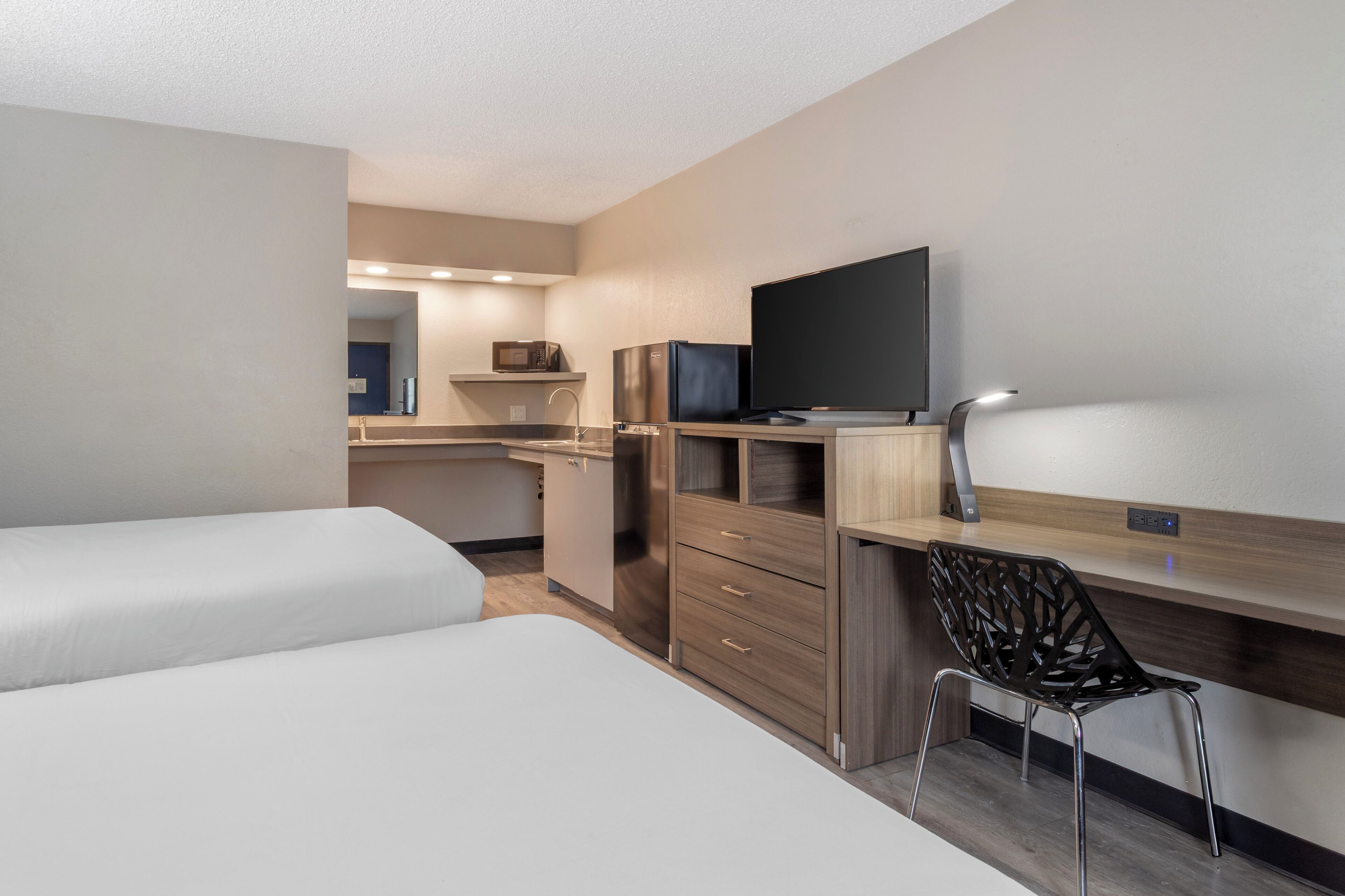 Een hotelkamer met een kitchenette, een televisie, een bureau met stoel en twee bedden.