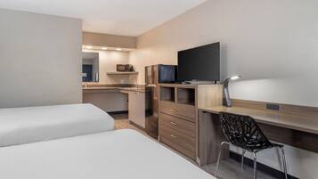 Een hotelkamer met een kitchenette, een televisie, een bureau met stoel en twee bedden.