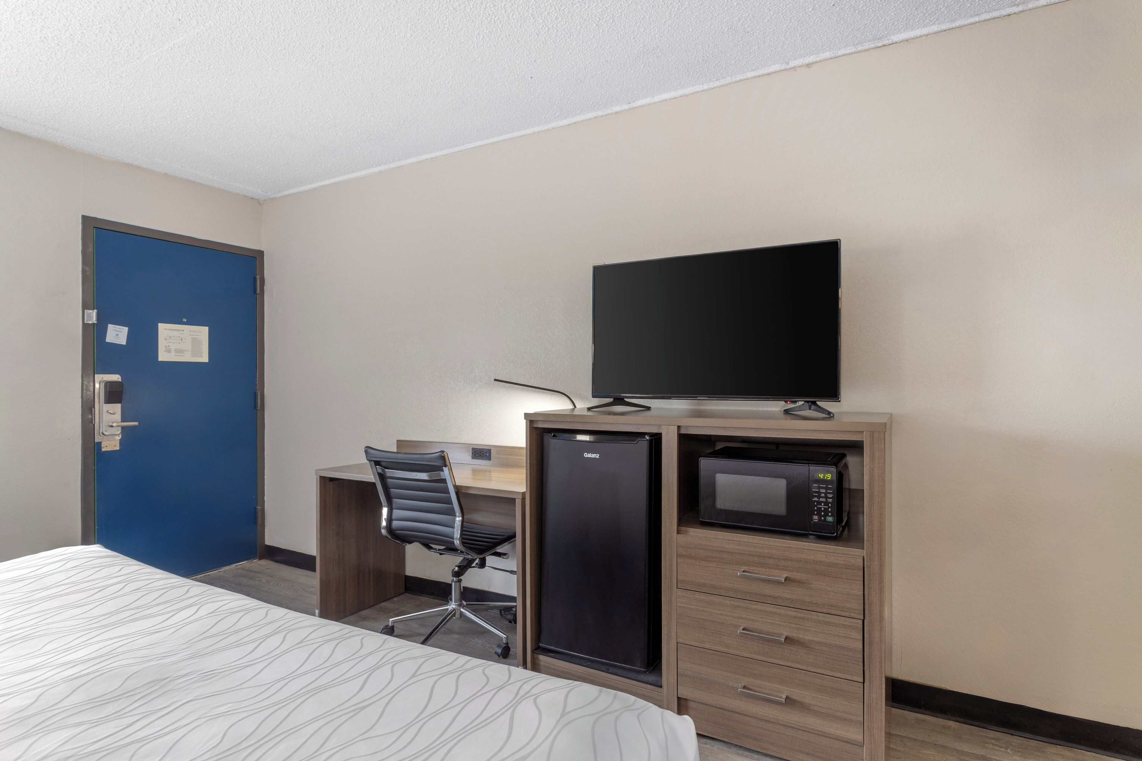 A hotel room with a bed, a desk with a computer and a microwave, and a television on top of the desk.