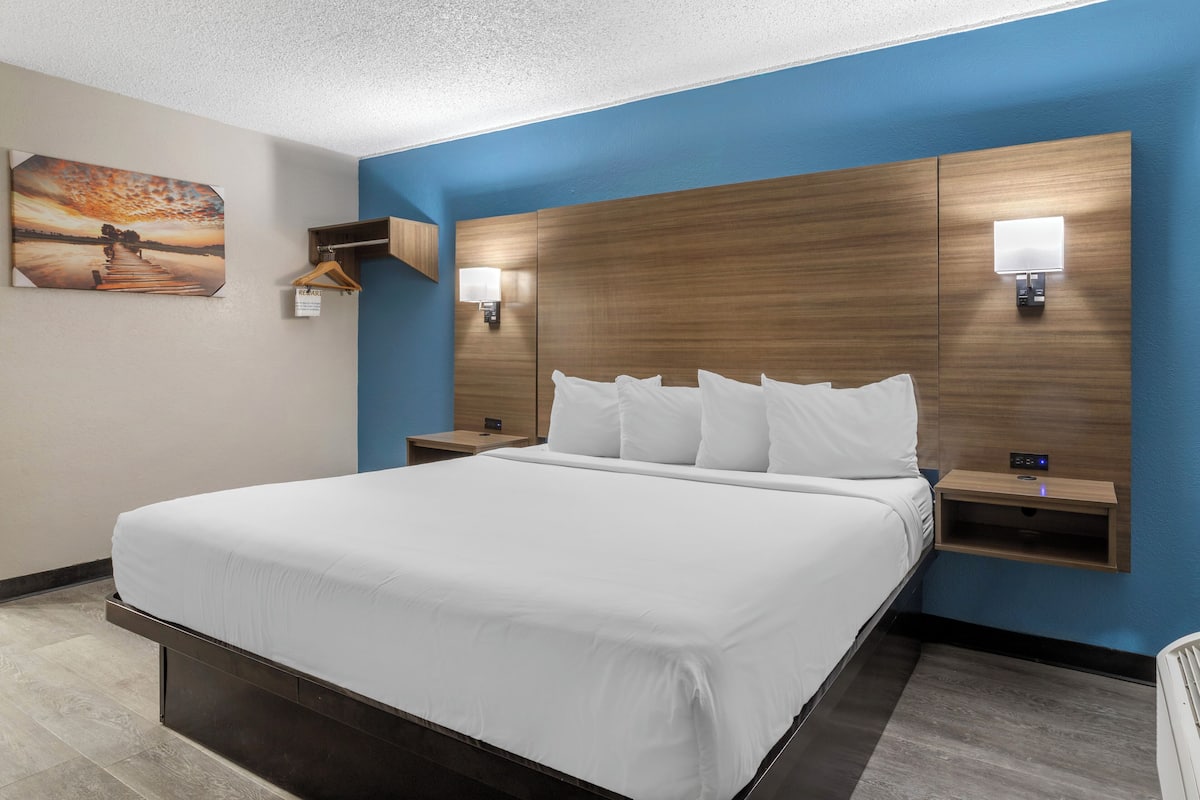 A hotel room with a large bed, two bedside tables, a wall-mounted light, and a painting on the wall.