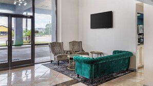 A modern lobby with a teal sofa, two armchairs, a small table, and a flat-screen TV on the wall.