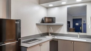A compact kitchen with a stainless steel refrigerator, a microwave on a shelf, a sink with a faucet, and a countertop.