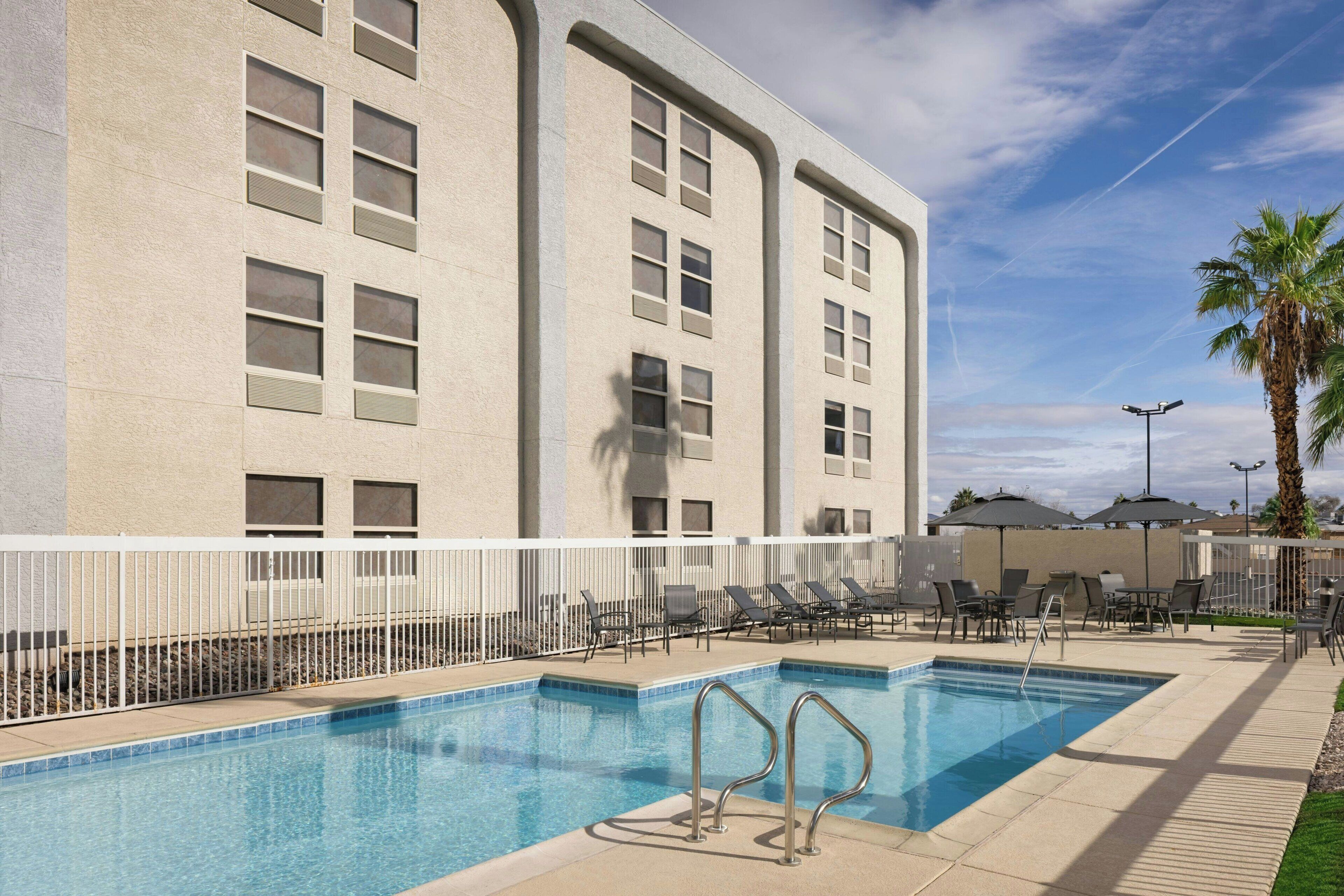 A swimming pool with a white fence, lounge chairs, and a palm tree.