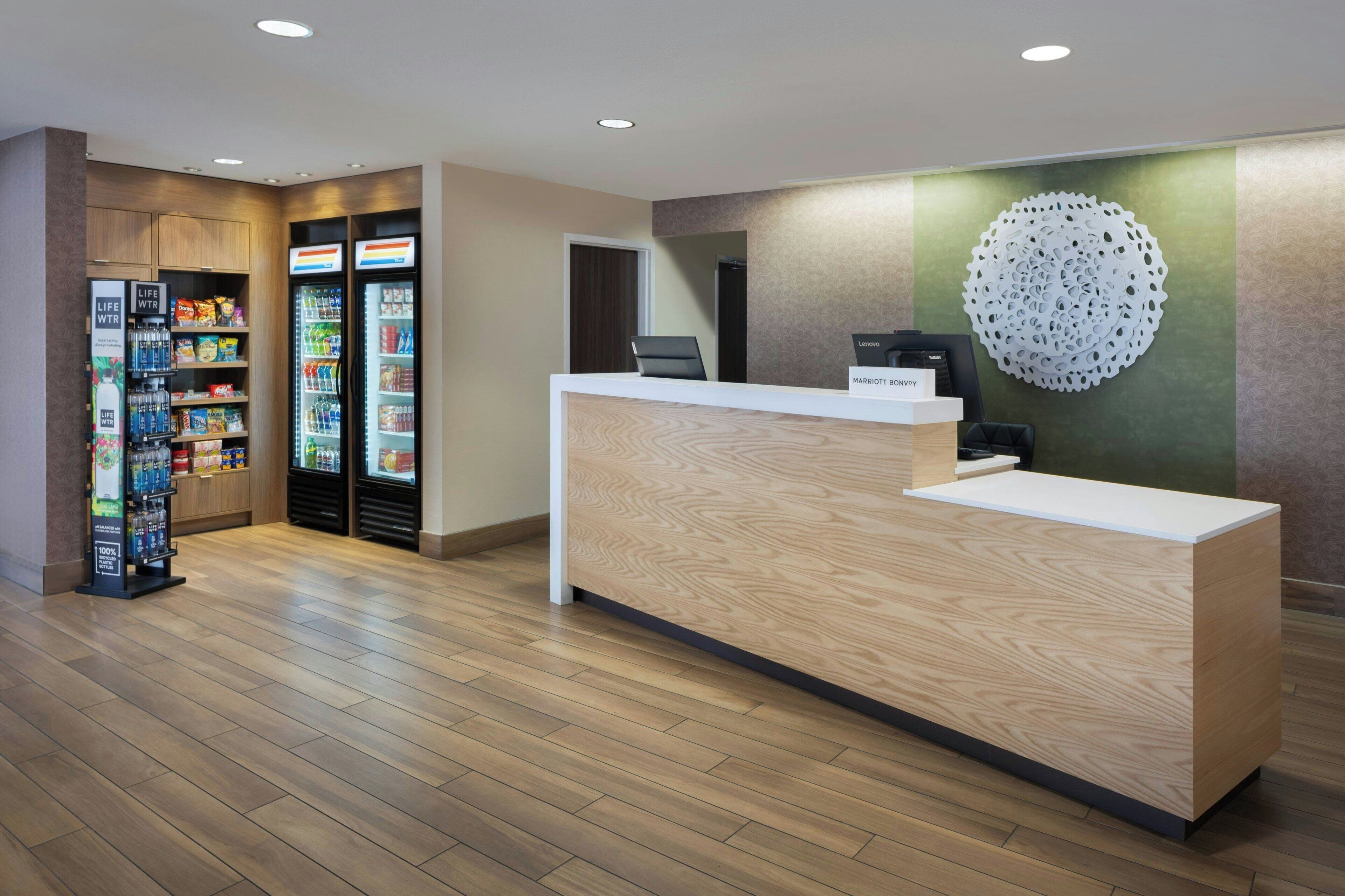 Un espace d’accueil d’hôtel avec un comptoir de réception en bois, un élément décoratif fixé au mur et des distributeurs automatiques.