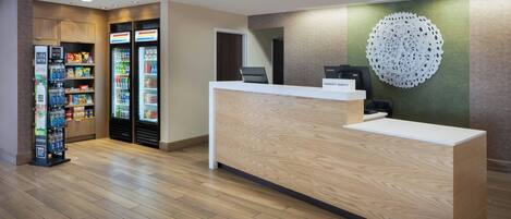 Un espace d’accueil d’hôtel avec un comptoir de réception en bois, un élément décoratif fixé au mur et des distributeurs automatiques.