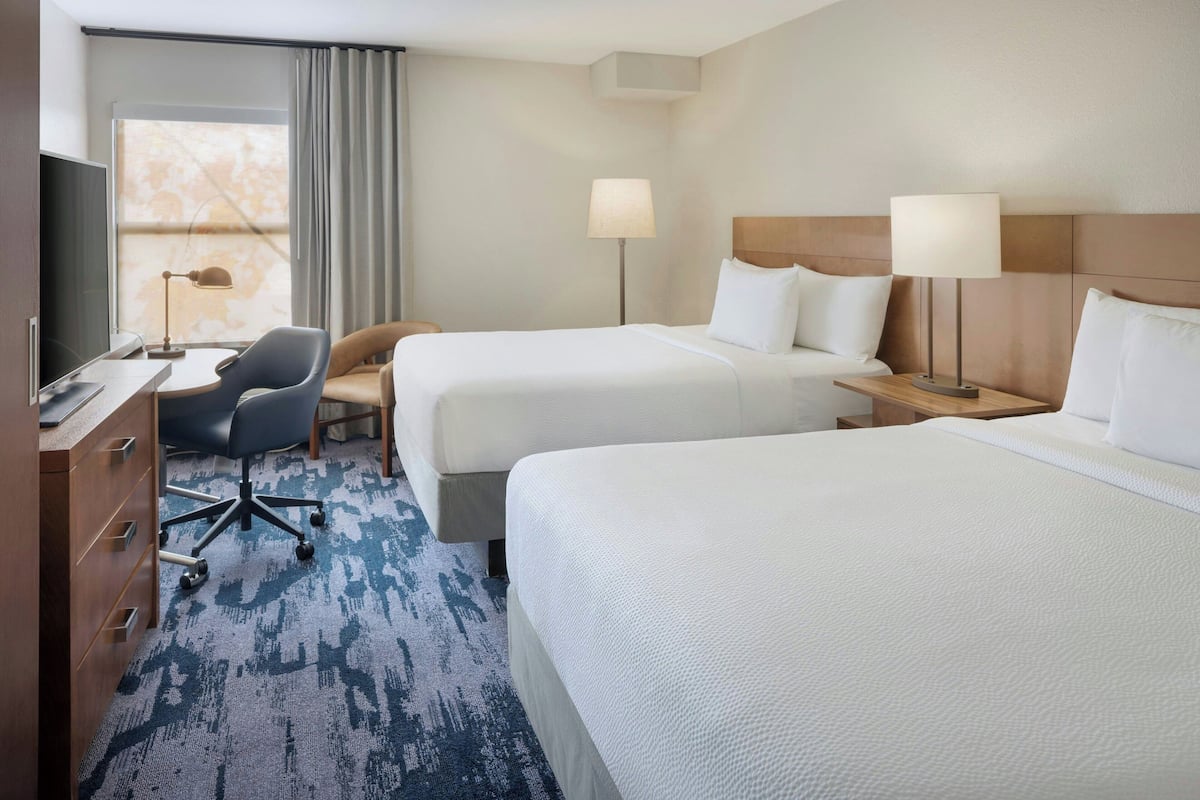 A hotel room with two beds, a desk, a chair, and a TV.