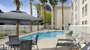 Un área junto a la piscina con sillones reclinables, una mesa y sombrillas.