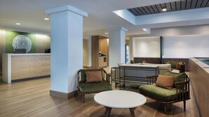 Un vestíbulo moderno con mostrador de recepción, zona de estar con sofás y una mesa redonda, y un área de piscina con vistas a la piscina.