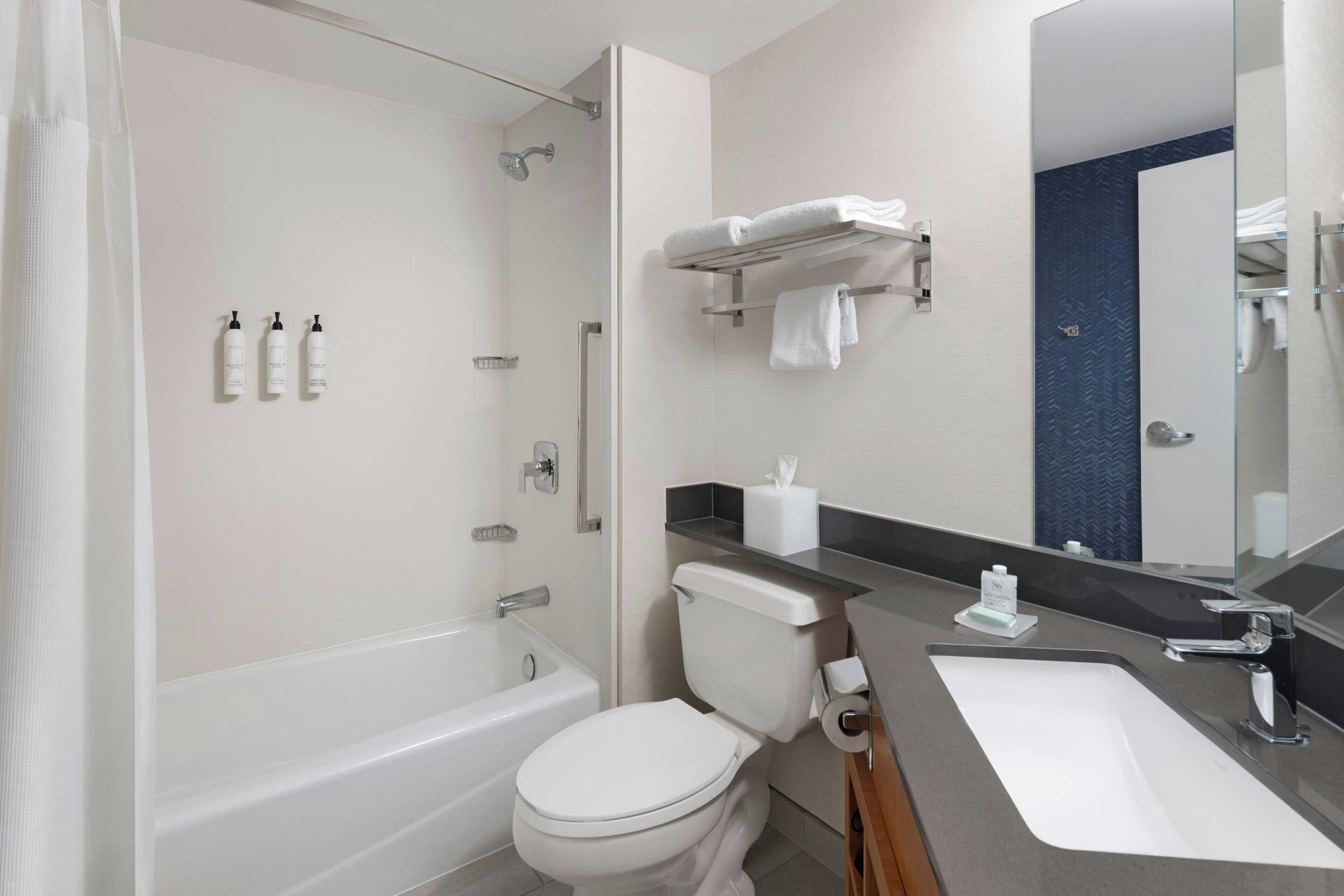 Ein modernes Badezimmer mit einer Badewanne, Toilette und Waschbecken. An der Wand befinden sich Pflegeprodukte und ein Handtuchhalter.