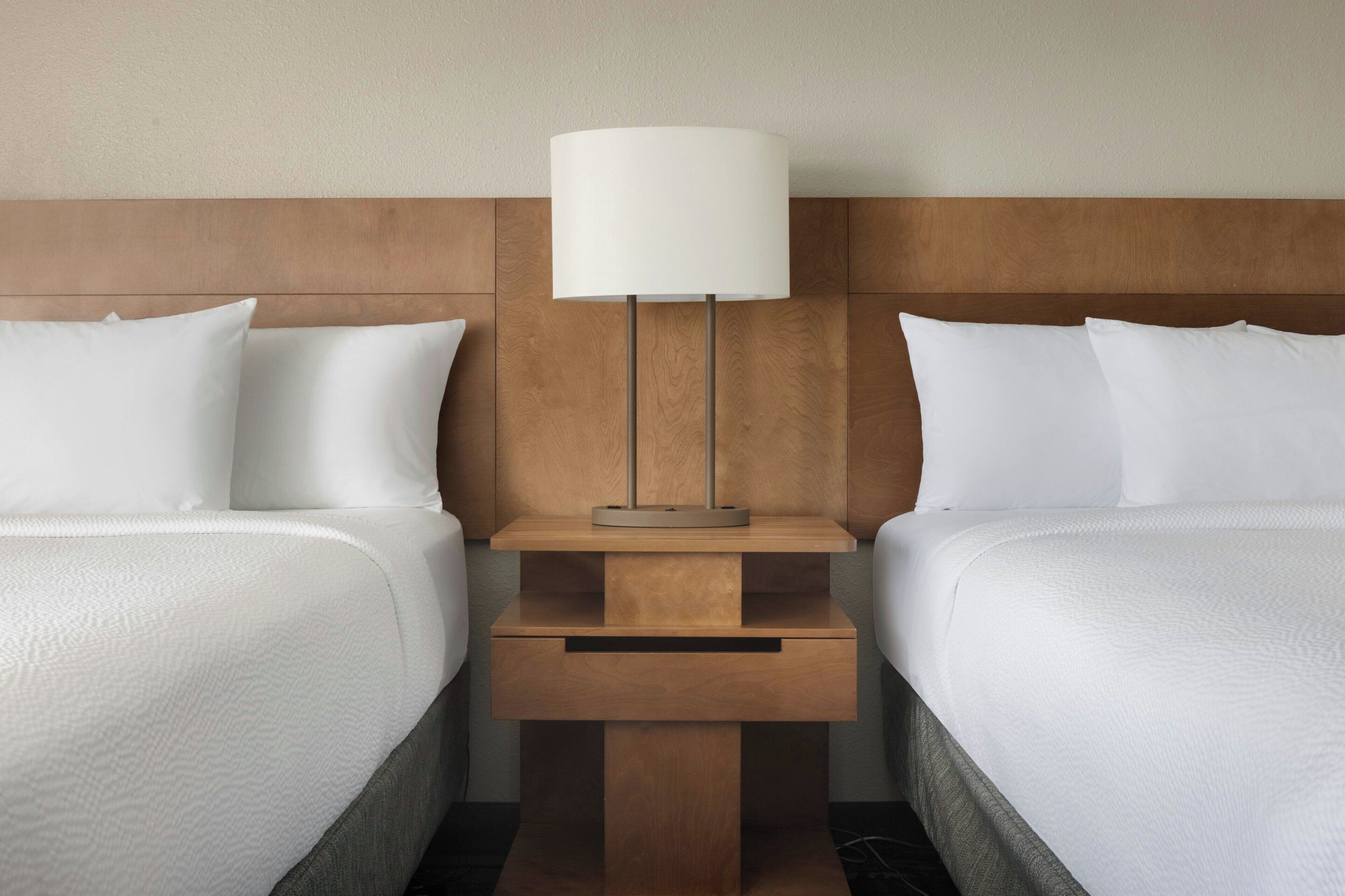 A hotel room with two beds, a nightstand with a lamp, and a small drawer unit.