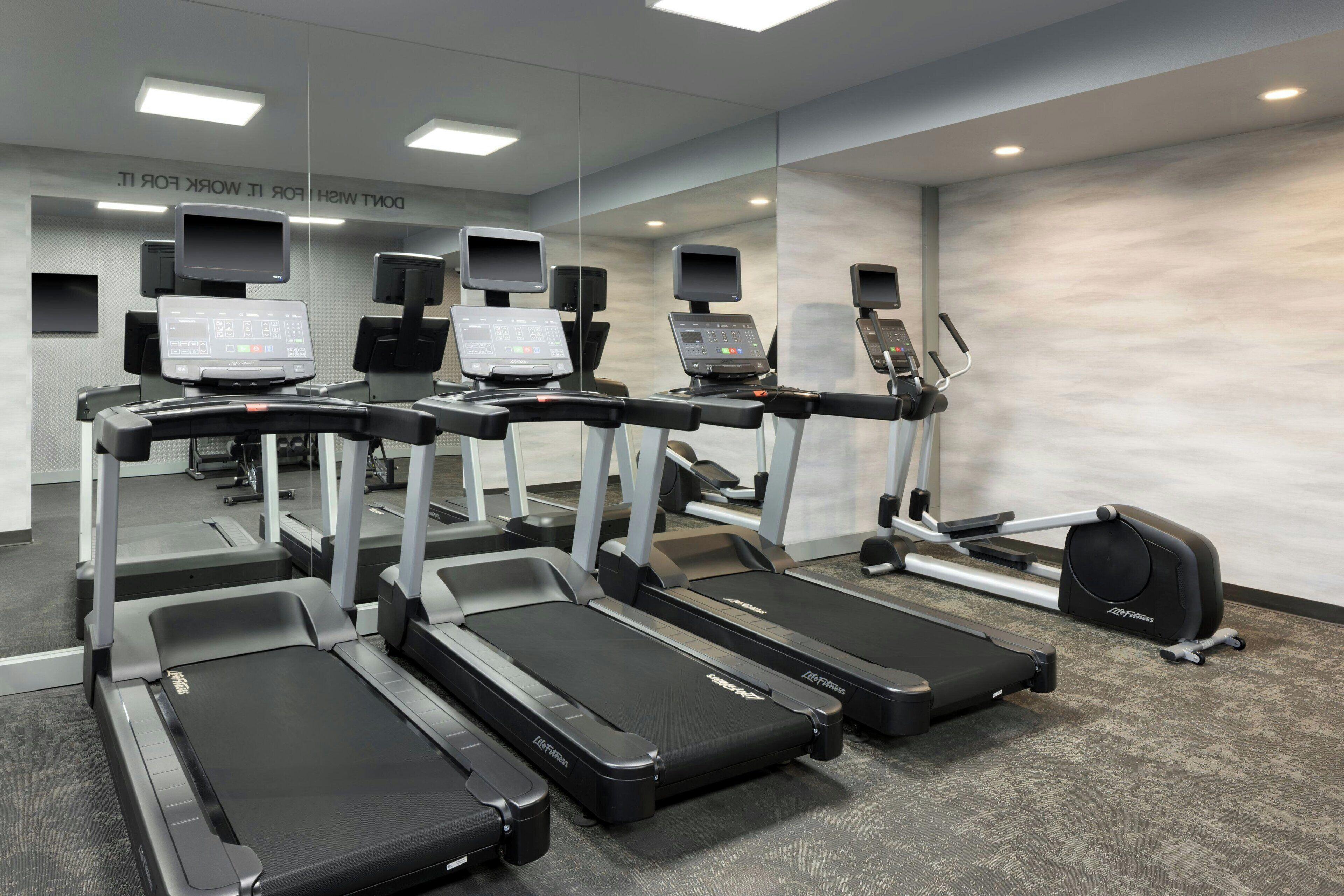 Academia com várias esteiras, bicicletas ergométricas e um banco de musculação.