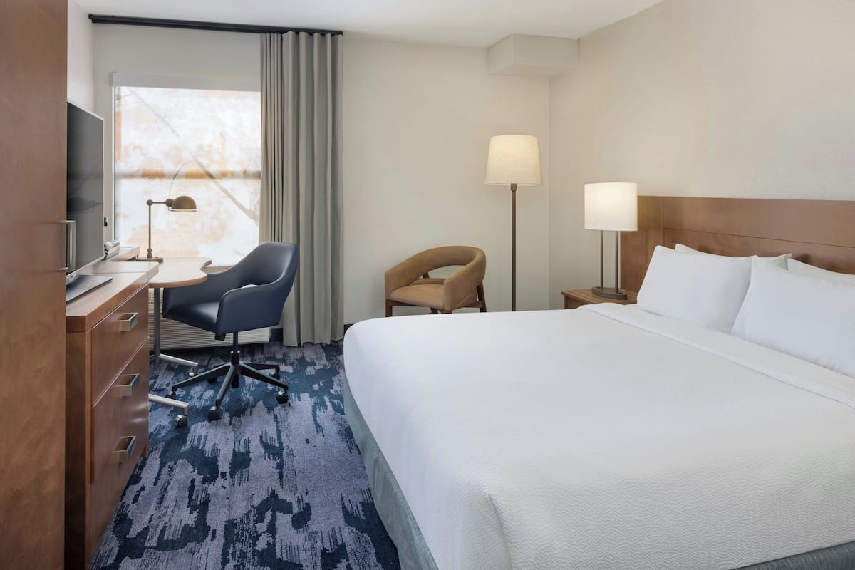 A hotel room with a large bed, a desk with a chair, a TV, and two lamps.