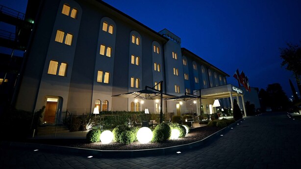A hotel with a modern facade, multiple windows, and outdoor seating area with umbrellas.