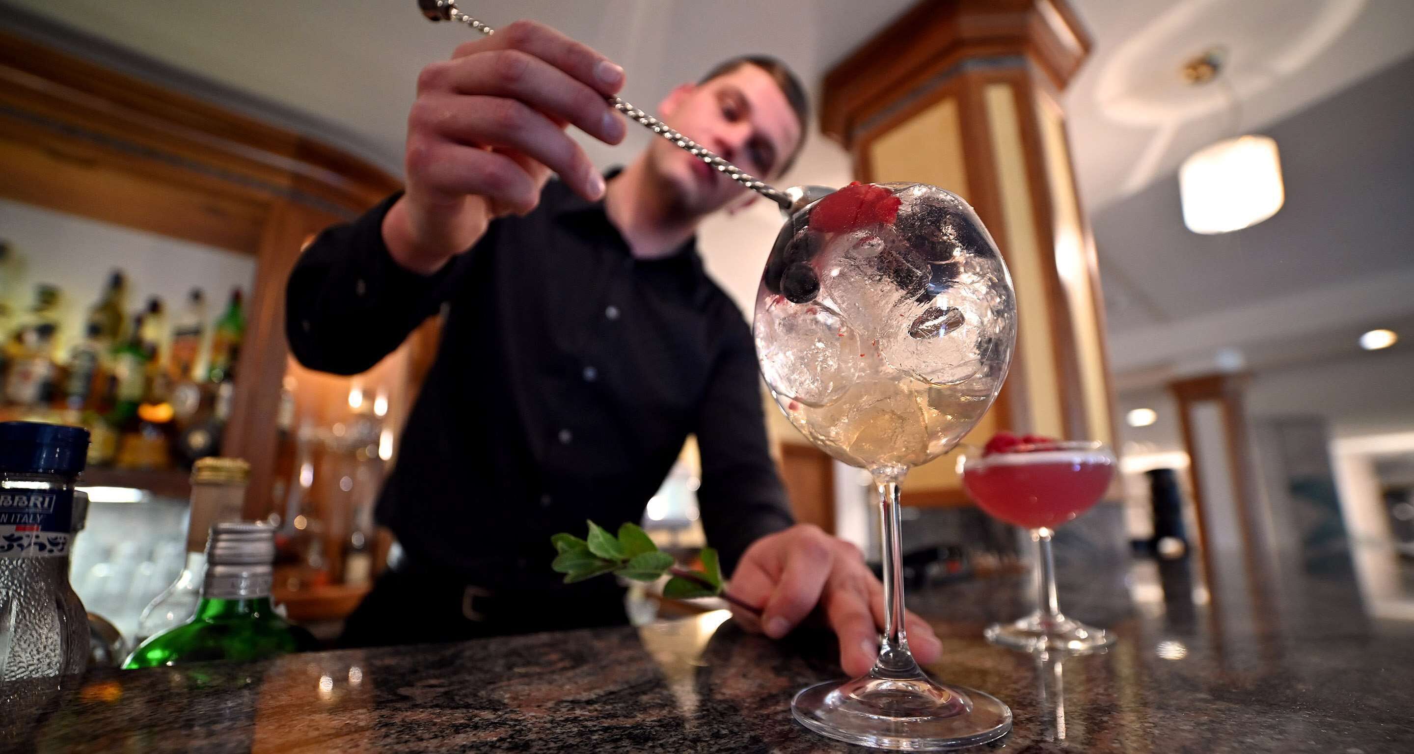 A bartender preparing a drink with a spoon in a glass.