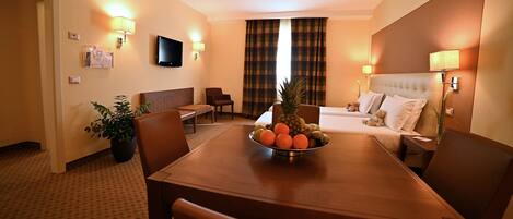 Una habitación de hotel con una mesa de comedor, sillas, un sofá, un televisor y una cama.