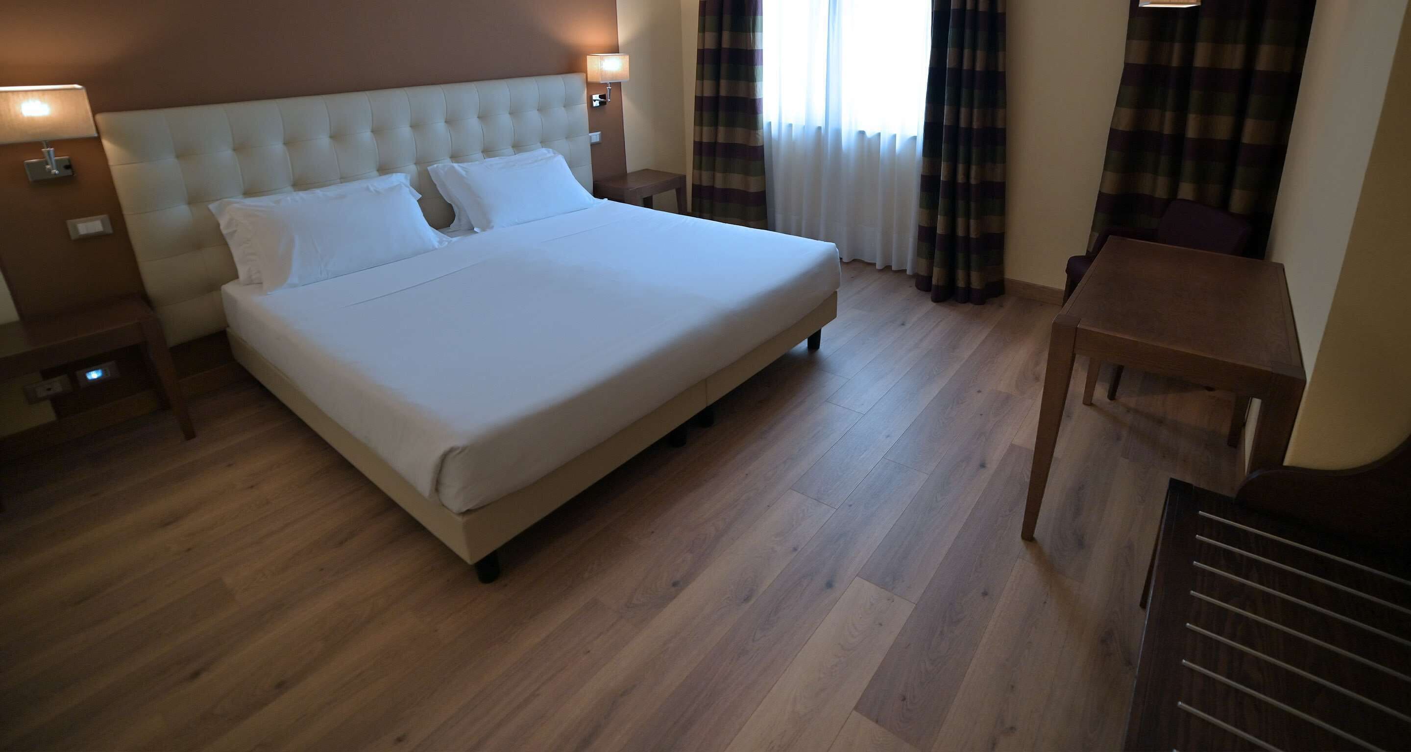 A neatly made bed with a padded headboard, a bedside table with a lamp, and a small wooden table.