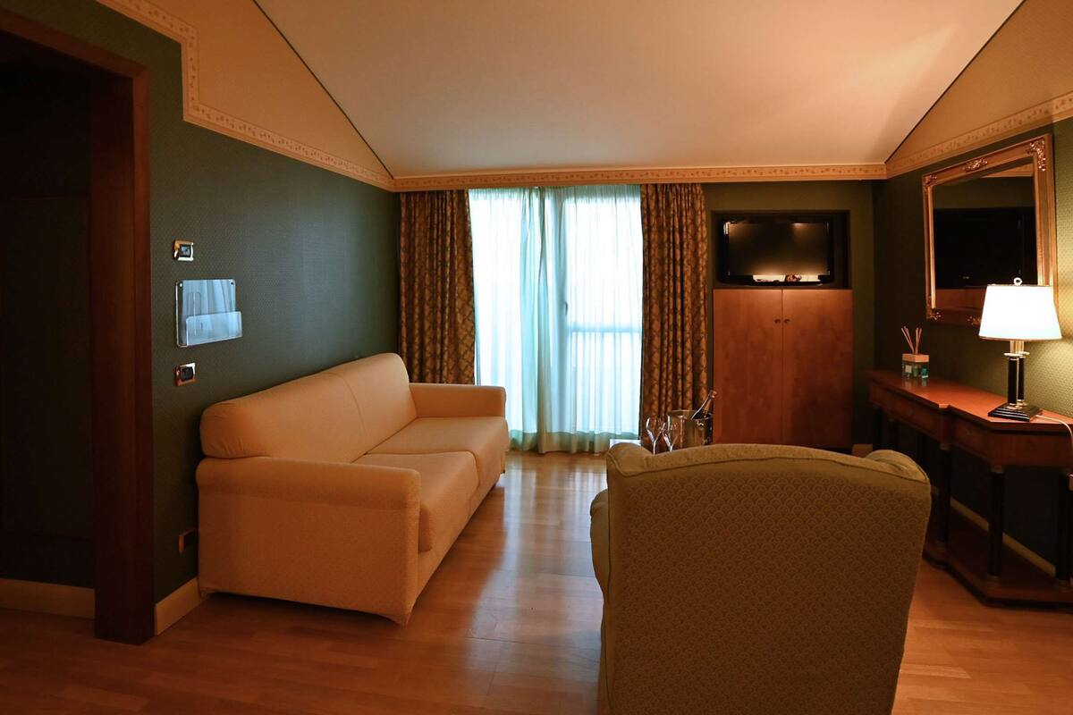 Habitación de hotel con cama, sofá, sillón, televisor y escritorio con lámpara.