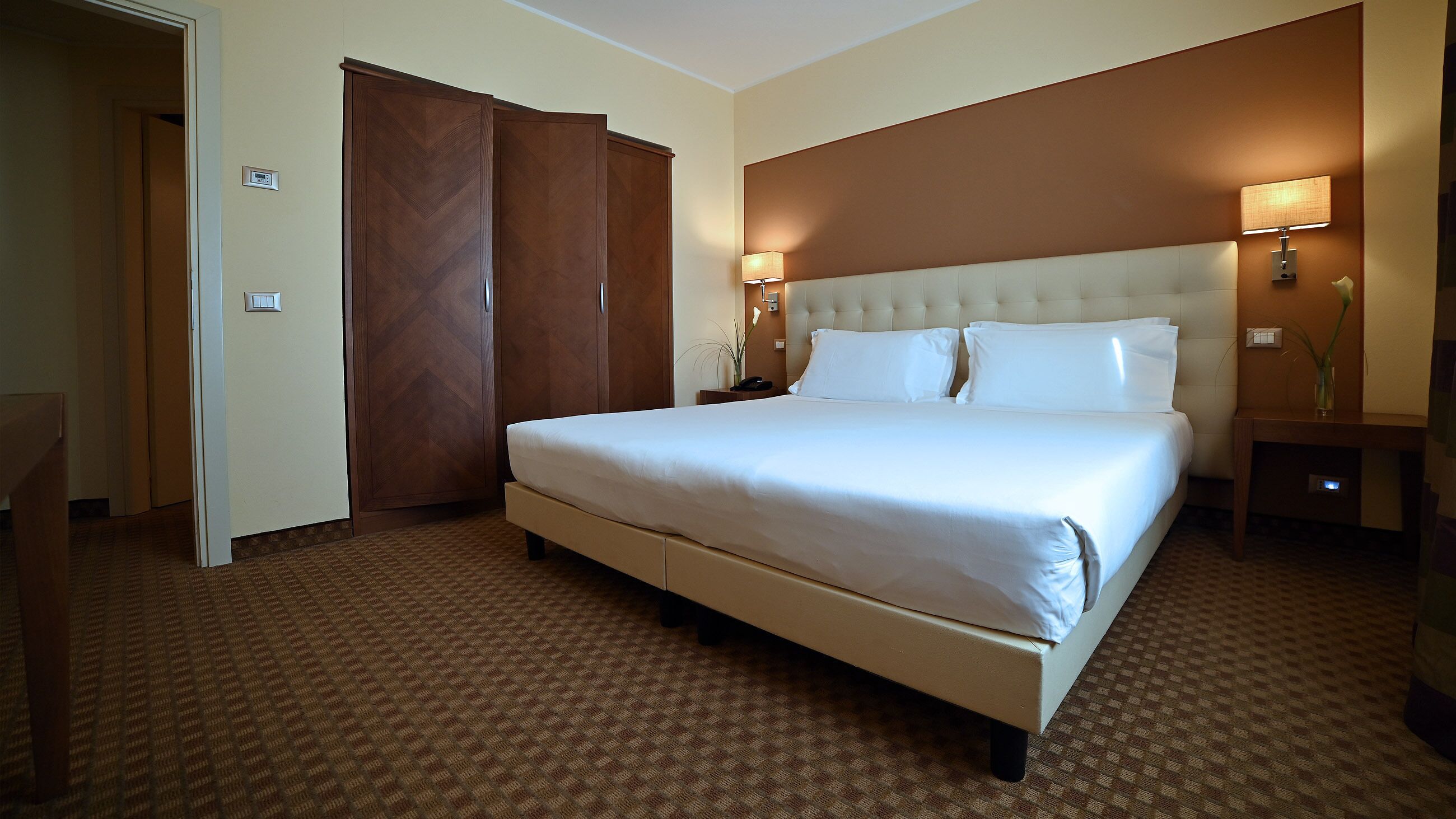 A hotel room with a large bed, a wardrobe, a bedside table, and a nightstand.