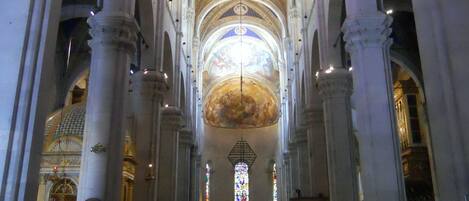 An interior with high vaulted ceilings, arched columns, and a central aisle leading to an altar.