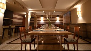 A dining area with a long wooden table set for a meal, surrounded by chairs with patterned cushions.
