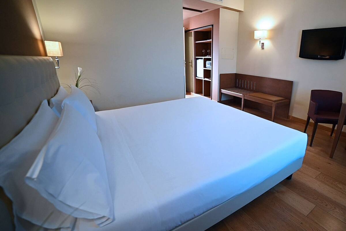 Habitación de hotel con cama, escritorio, silla, televisor y una mesita con fruta.