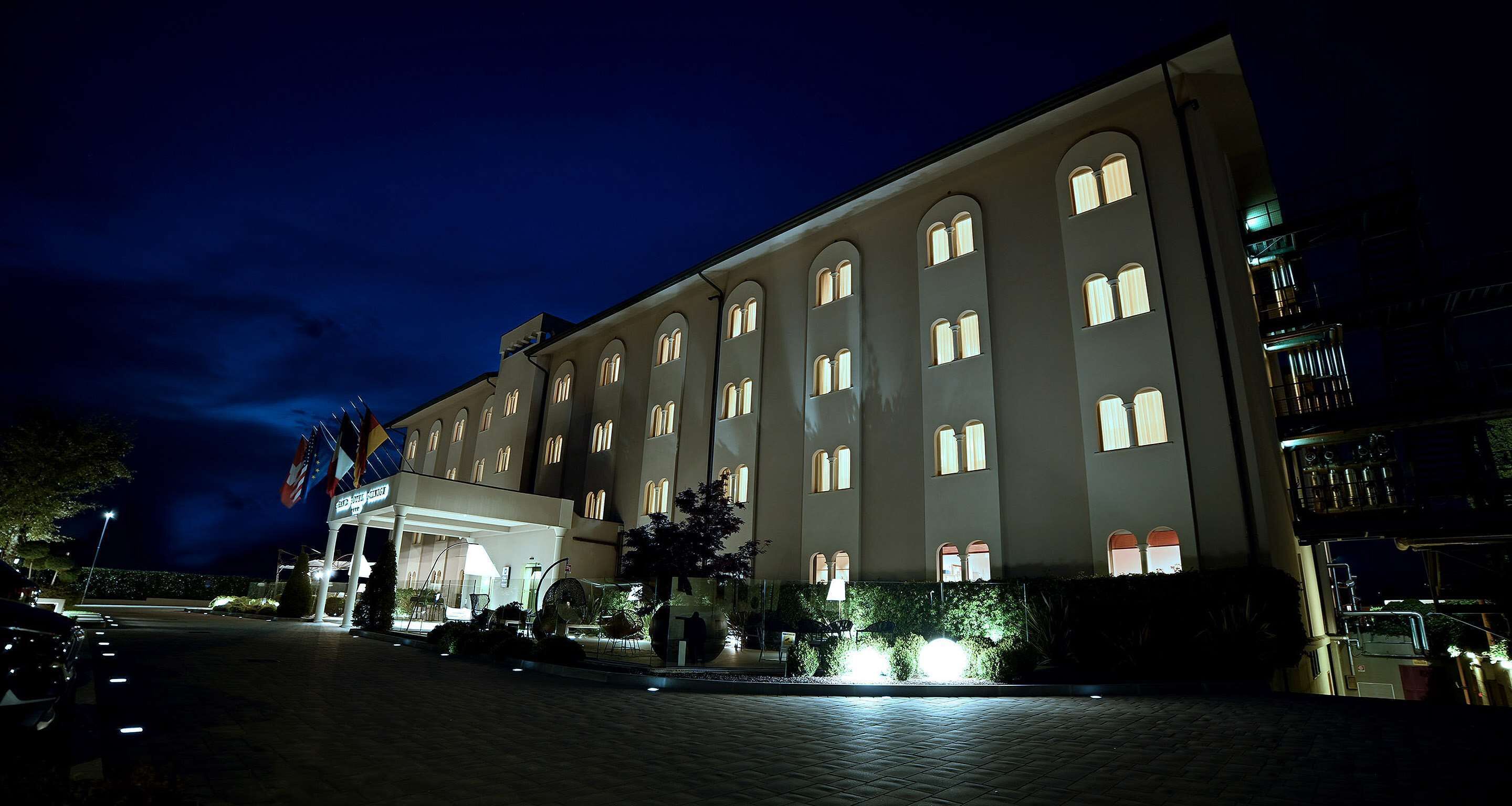 Un gran hotel de varios pisos con ventanas arqueadas, una entrada cubierta y un camino de acceso pavimentado.