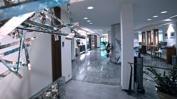 A modern hotel lobby with a marble floor, a reception desk, and a staircase.
