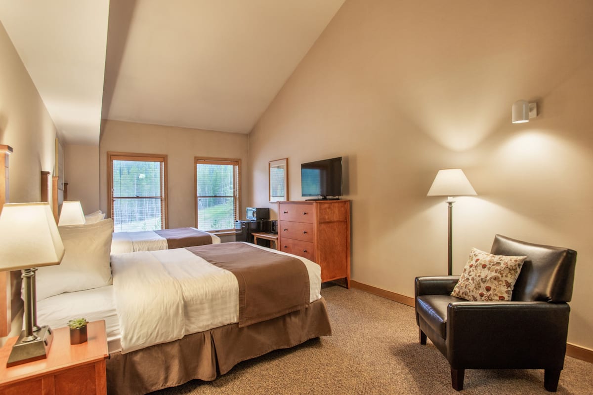 Une chambre d’hôtel avec deux lits, un bureau avec une lampe, une chaise, une commode, une télévision et une fenêtre.