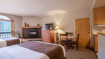 A hotel room with two beds, a fireplace, a television, a desk with a chair, and a door.