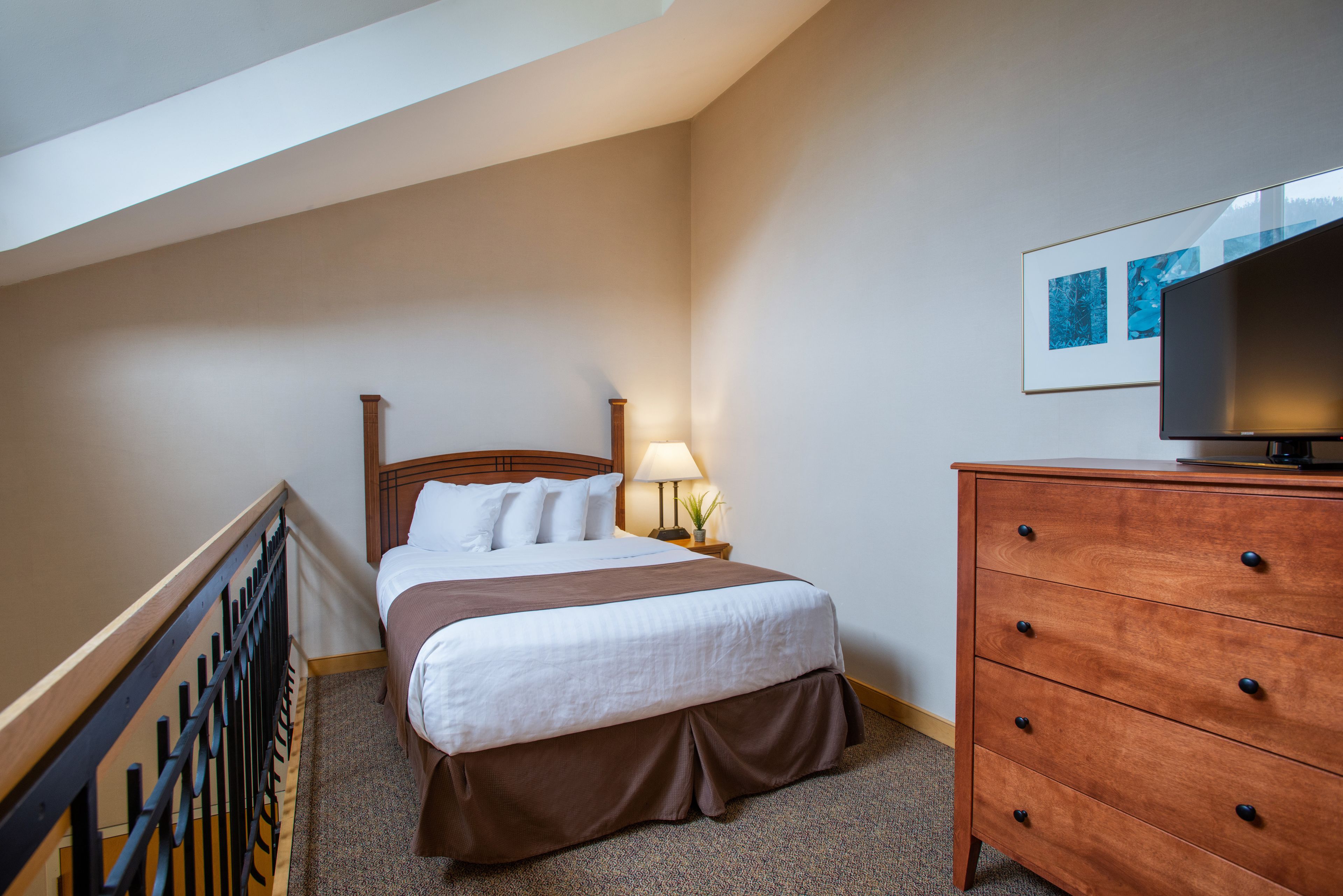 A hotel room with a bed, a dresser, a TV, and a lamp.
