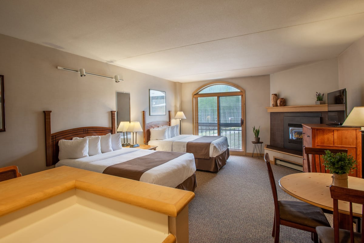 Une chambre d’hôtel avec deux lits, une table à manger, un téléviseur et une cheminée.
