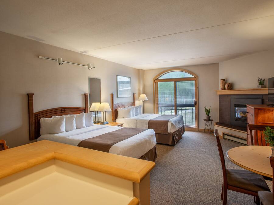 A hotel room with two beds, a dining table, a TV, and a fireplace.
