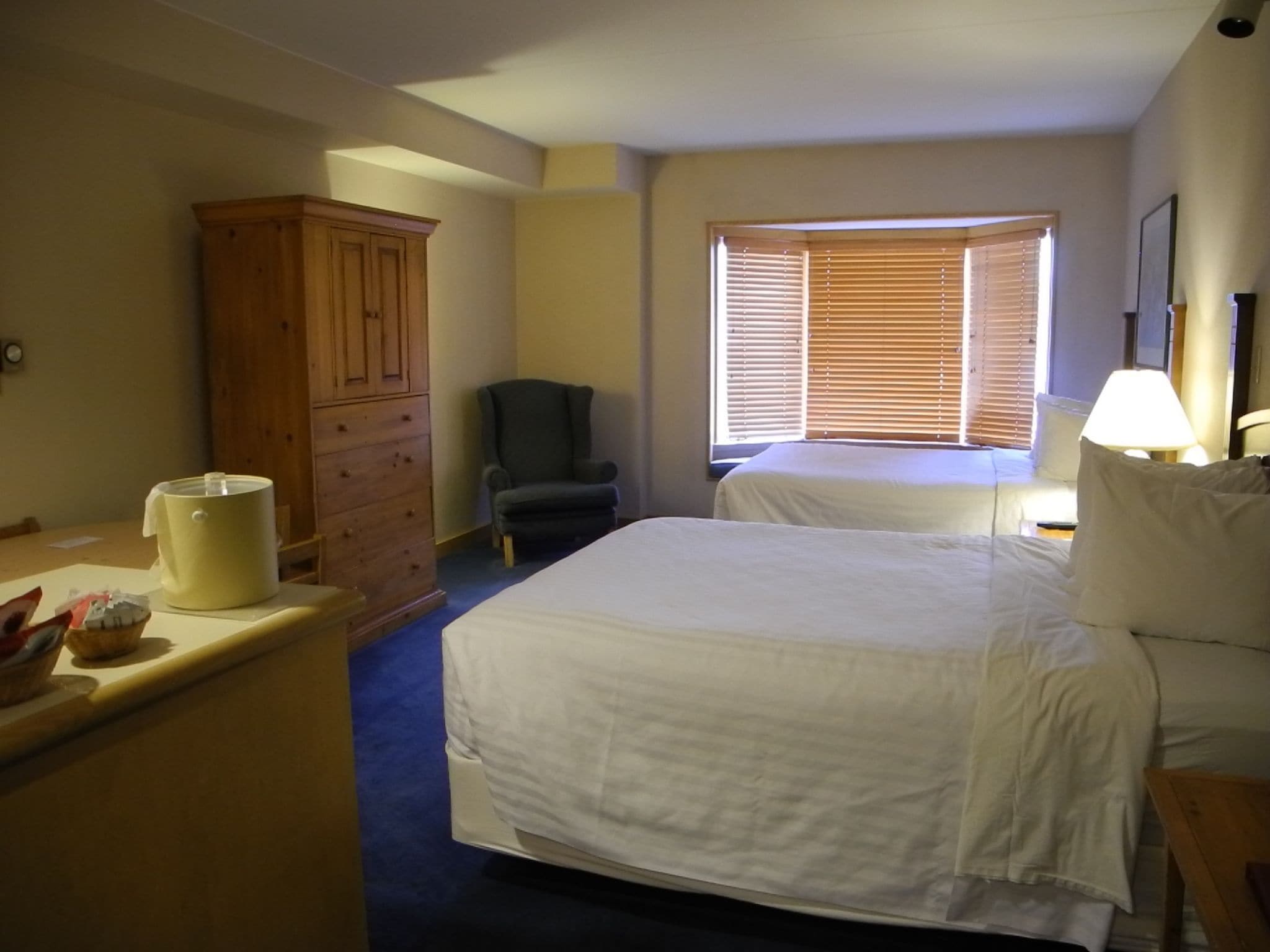 A hotel room with a large bed, a chair, a wooden cabinet, and a window with blinds.
