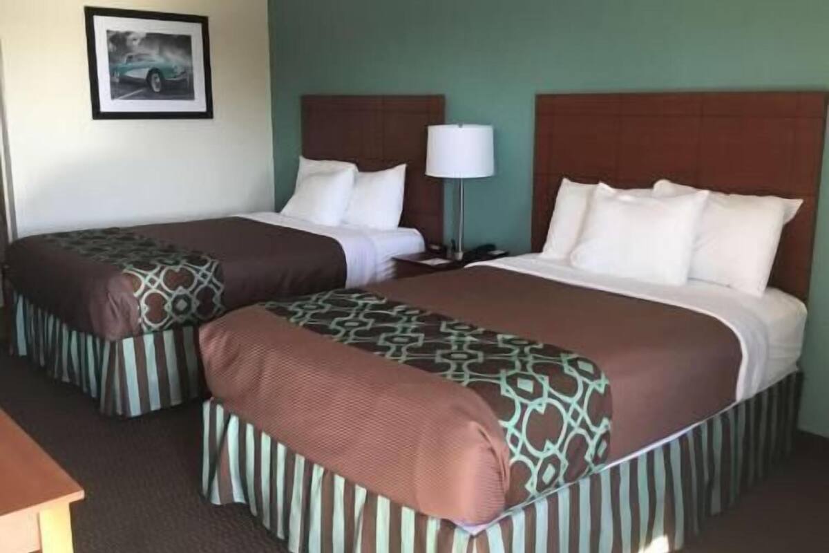 A hotel room with two beds, a nightstand with a lamp, a framed picture on the wall, and a desk.
