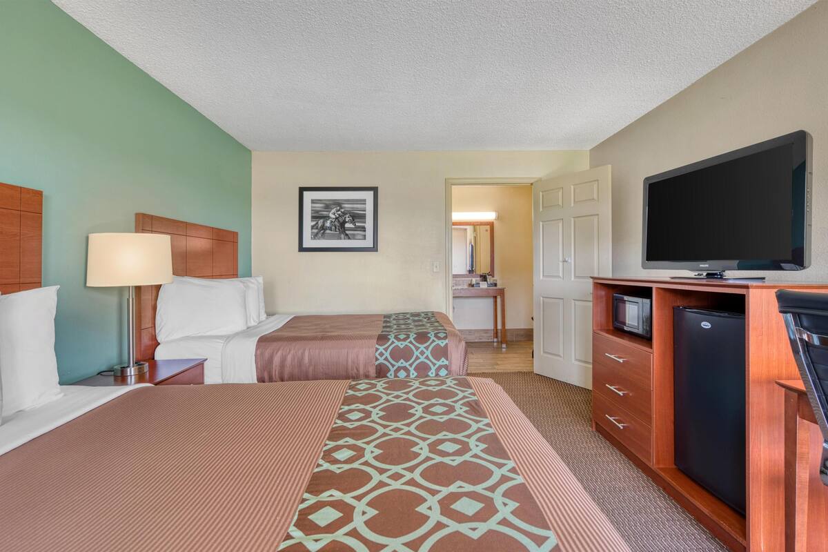A hotel room with two beds, a TV, a refrigerator, and a desk with a lamp.