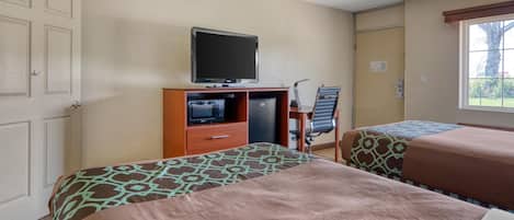 A hotel room with two beds, a television, a desk with a computer, and a window.