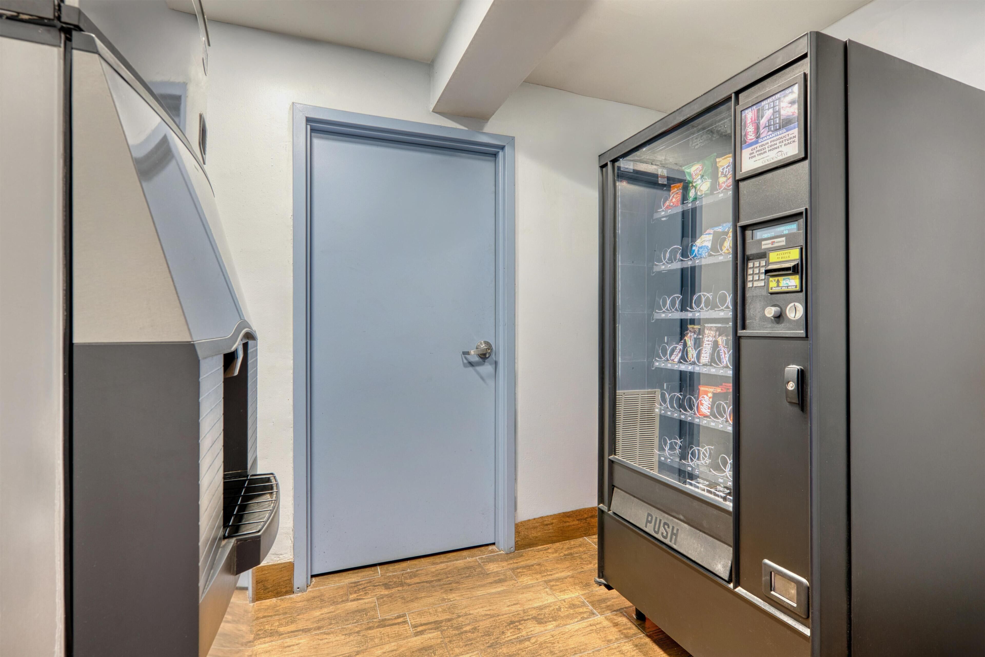 A hallway with a blue door, a vending machine, and a kitchenette area.