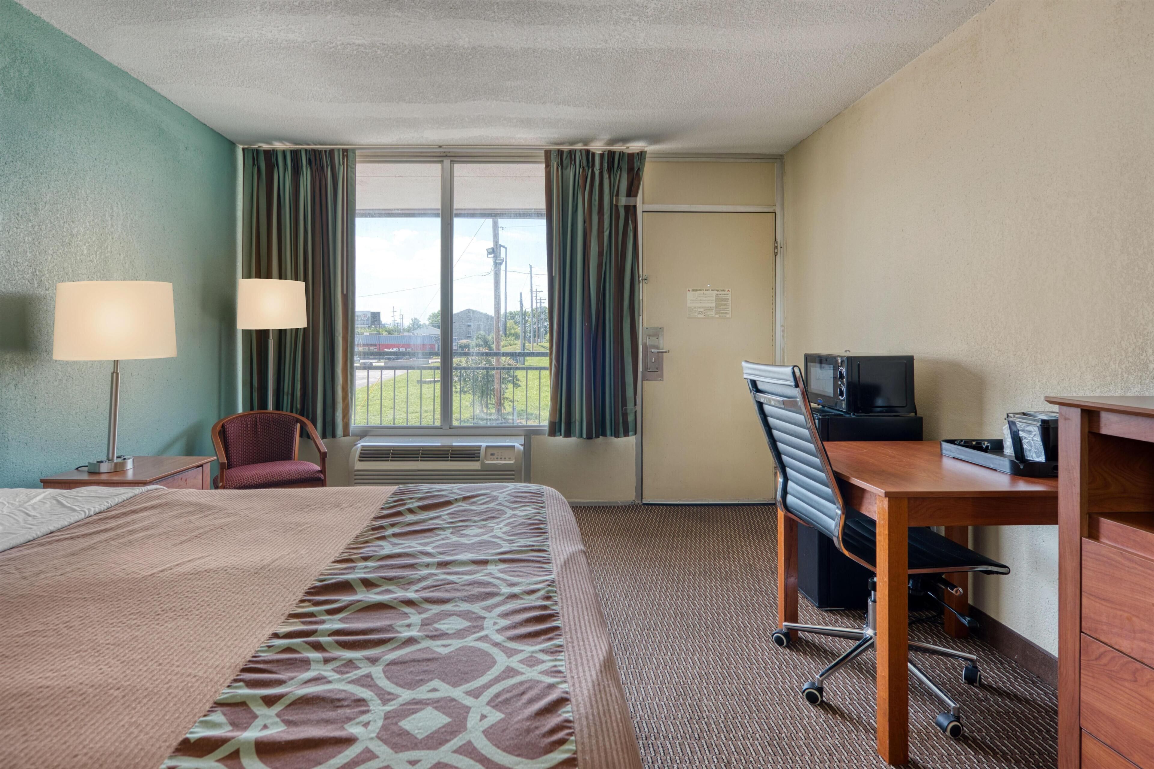 Een hotelkamer met een bed, bureau, stoel, televisie en een raam met gordijnen.