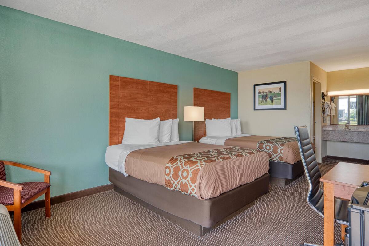 A hotel room with two beds, a desk, a chair, and a bathroom visible through an open door.